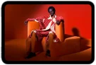iPad mini displayed, front view, screen showing a vivid screen with a person in an orange suit, sitting on an orange chair, placed in an orange room