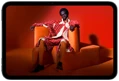 iPad mini displayed, front view, screen showing a vivid screen with a person in an orange suit, sitting on an orange chair, placed in an orange room