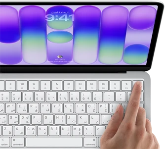 جهاز MacBook Neo، لون فضي، يعرض شاشة تسجيل الدخول، إصبع شخص على مستشعر بصمة الإصبع في الزاوية العلوية اليسرى من لوحة المفاتيح