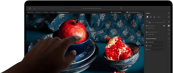 جهاز MacBook Pro مع شاشة PROLED XDR يعرض صورة ثابتة لثمار الرمان وقطع خزفية ومنسوجات زرقاء، مع يد تمتد نحو الشاشة للتفاعل مع العمل الفني