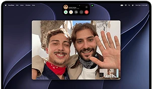MacBook Pro with PROLED XDR Display, silver color, display shows a video call in progress with two people in a sunlit town waving to a person at home